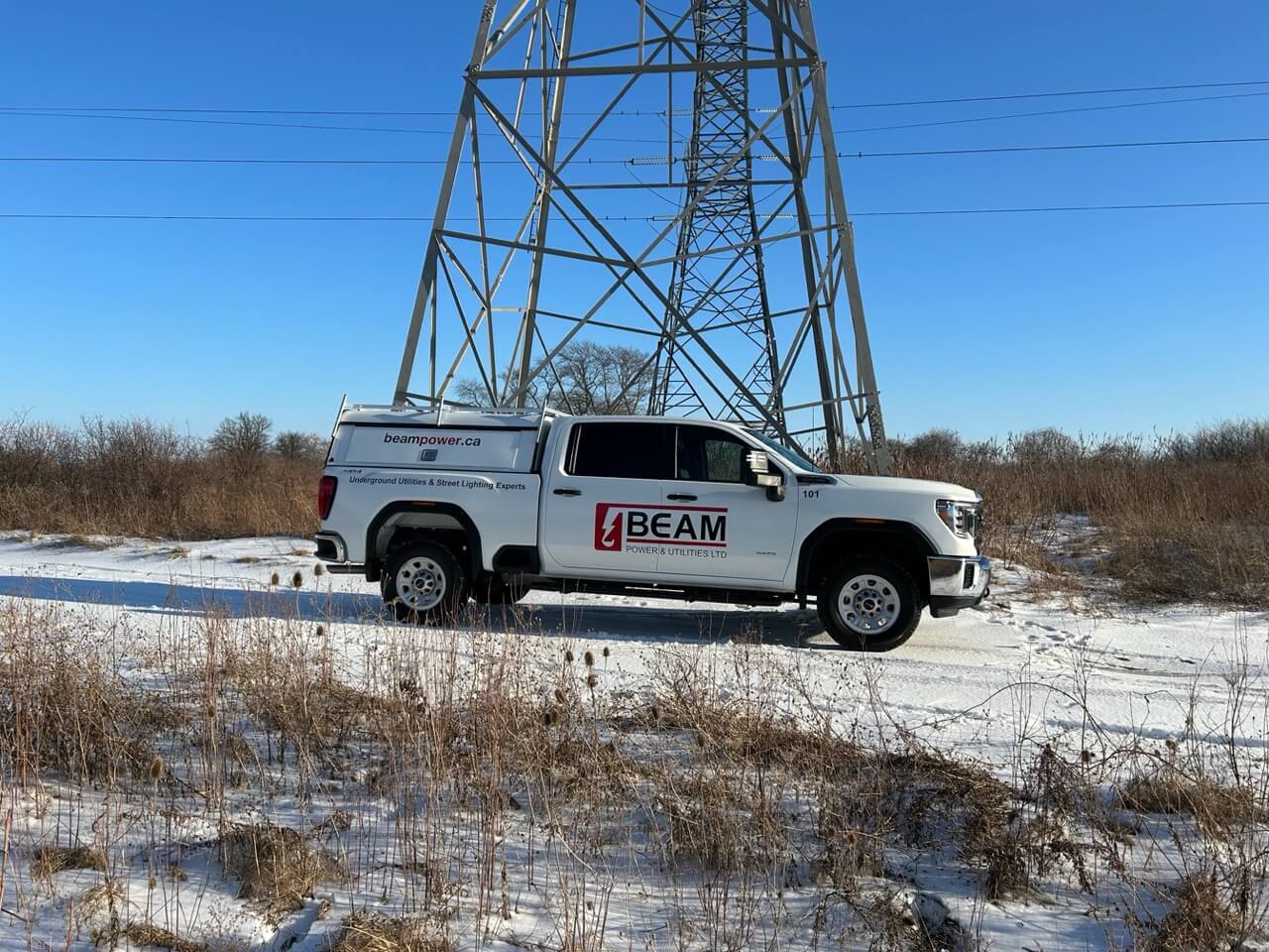 White Beampower work pickup truck in front of transmission tower on a snowy path